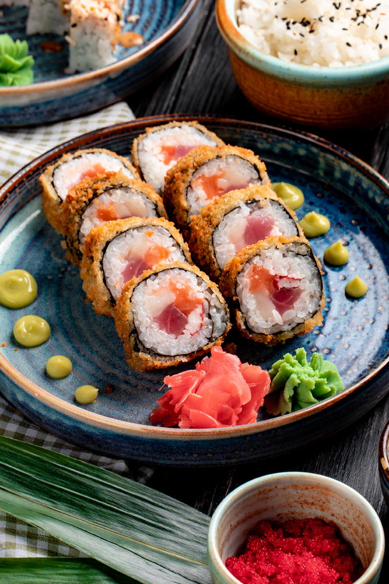 side view of sushi roll with crab and tuna on a plate with ginger and wasabi on wooden background